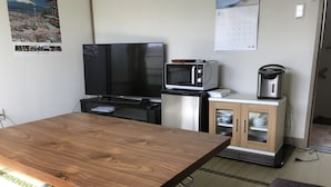 A compact kitchen with a wooden table, a TV, a microwave, and a coffee maker. - Tamaki (Fujiyoshida)