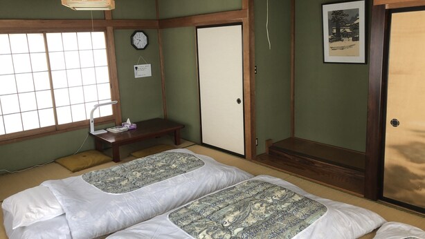 A traditional Japanese room with tatami flooring, two tatami mats, a wooden bench, a clock, and a framed picture on the wall. - Tamaki (Fujiyoshida)