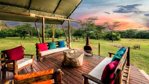 Un espace extérieur aménagé avec une terrasse en bois, un canapé agrémenté de coussins colorés, une table rustique et un grand pot en terre cuite.