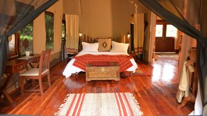 Une pièce aménagée avec une tente, un lit, un bureau en bois, une chaise et une petite commode.