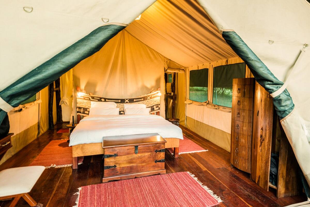 Une pièce aménagée avec une tente, un lit, des meubles en bois et un tapis rouge.