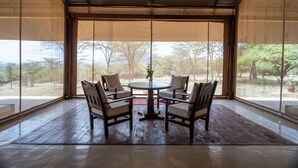 Un espace extérieur aménagé, abrité et doté d’une table et de chaises en bois, de grandes fenêtres et d’une vue sur les arbres.