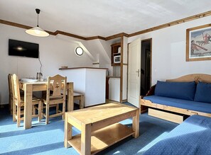 A compact living space with a dining area, a sofa, a TV, and a kitchenette.