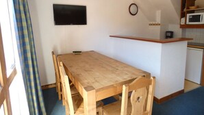 A compact kitchen with a wooden dining table and chairs, a flat-screen TV, a clock, and a microwave. - Athamante 60 - Large duplex, close to slopes and shops (LES AVANCHERS VALMOREL)