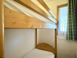 A bunk bed with a wooden headboard and a window with curtains.