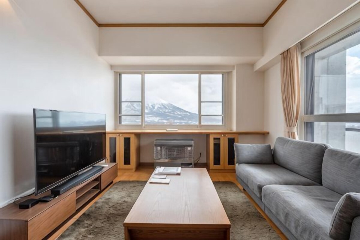 Una sala de estar moderna con televisor de pantalla plana, un sofá, una mesa de centro y un ventanal con vistas a la montaña.