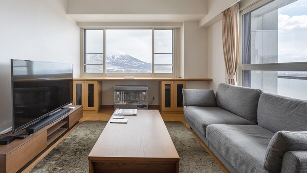 Un salon moderne doté d’un téléviseur à écran plat, d’un canapé gris, d’une table basse en bois et offrant une vue sur une montagne grâce à de grandes fenêtres.