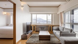 Une chambre d’hôtel moderne équipée d’un lit, d’un canapé, d’une télévision, d’une cheminée et de grandes fenêtres donnant sur les montagnes.