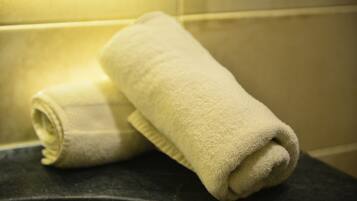 Two rolled towels on a dark surface in a bathroom with tiled walls.