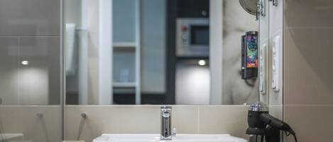 A bathroom with a white sink, a mirror, and a hairdryer on the counter.