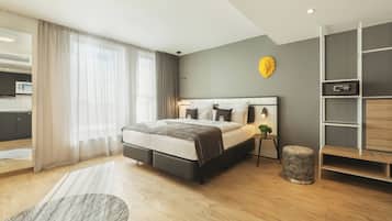 Un dormitorio moderno con cama, mesitas de noche, un reposapiés redondo pequeño, un estante en la pared y vista al área de la cocina.