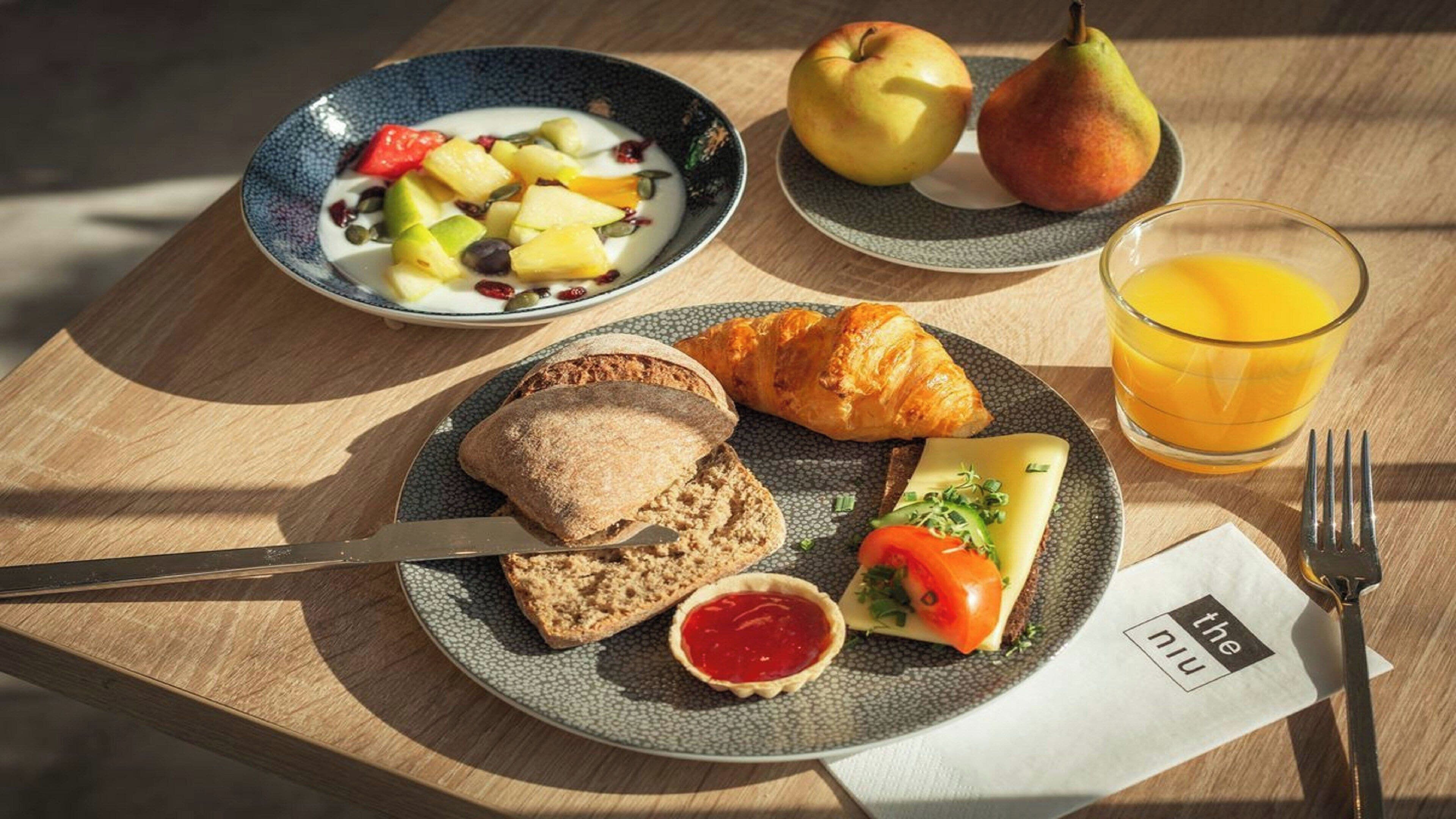 Een ontbijtsetting met een bord toast, een croissant, een kleine salade en een glas sinaasappelsap.