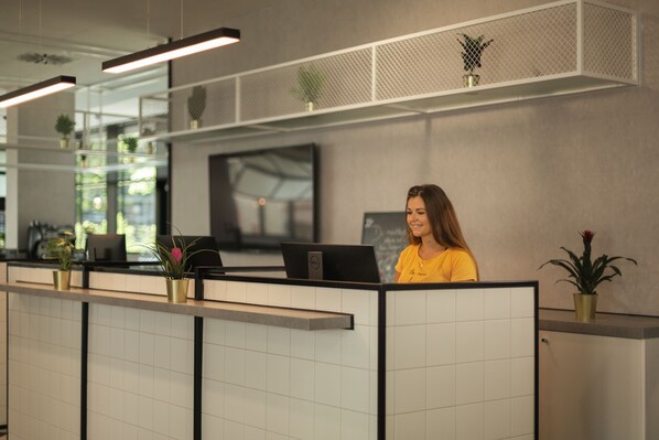 Un área de recepción de diseño moderno, con mostrador de recepción, televisor de pantalla plana y plantas en macetas.