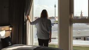 Una habitación con un ventanal grande, una cama, una mesita de noche y una lámpara.