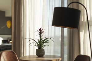 A round table with a potted plant, a lamp, and a chair in a room with a window and curtains. - Holiday Inn - the niu, Leo Nuremberg by IHG (Nuremberg)