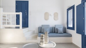 A modern interior with a white staircase, a blue door, a seating area with cushions, and two tall vases on a small table.
