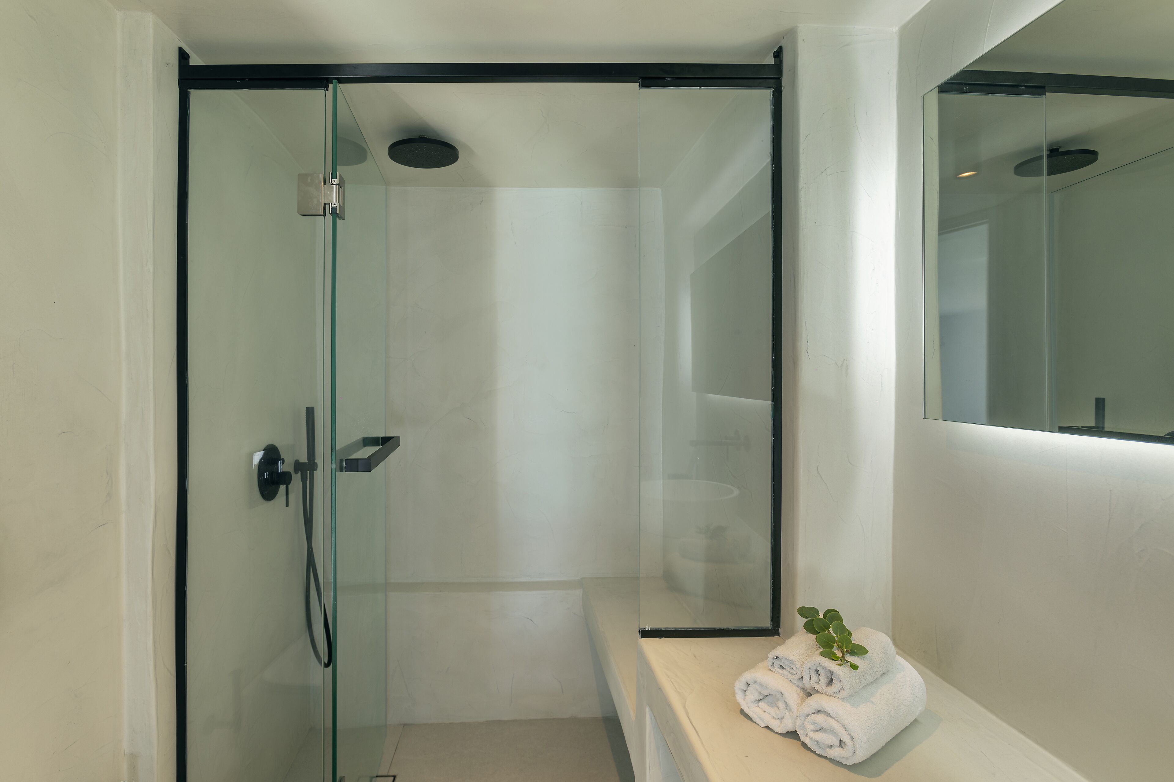 A modern bathroom with a glass-enclosed shower, a white sink, and a bench with towels.