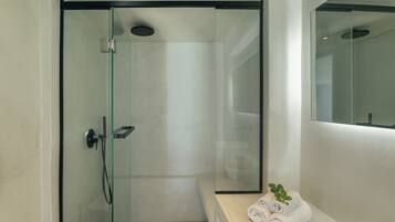 A modern bathroom with a glass-enclosed shower, a white sink, and a bench with towels.