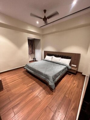 Una camera da letto con un letto, pavimento in legno, ventilatore a soffitto e comodino.