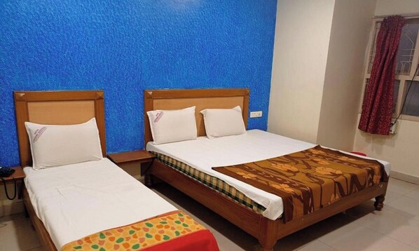 A hotel room with two beds, a blue textured wall, a window with red curtains, and a bedside table with a phone. - Hotel Lakshmi Residency (Visakhapatnam)