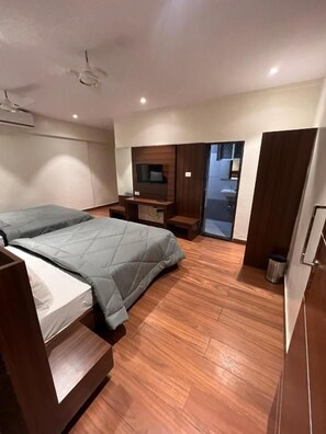 Una camera da letto moderna con un letto, pavimento in legno, una TV e una porta scorrevole che dà su un bagno.
