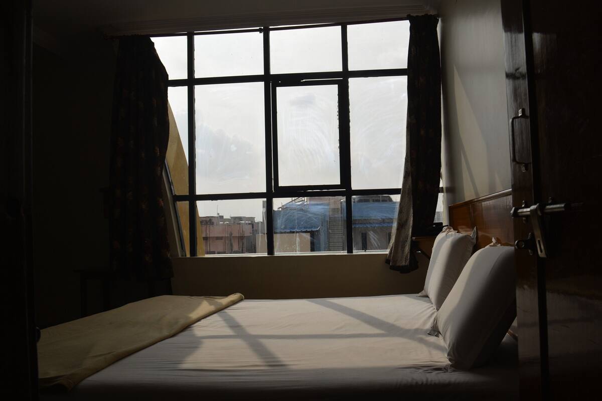 Une chambre avec un lit, une fenêtre et une vue sur les bâtiments environnants.