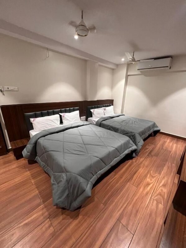A bedroom with two beds, wooden flooring, a ceiling fan, and an air conditioning unit. - Hotel Lakshmi Residency (Visakhapatnam)