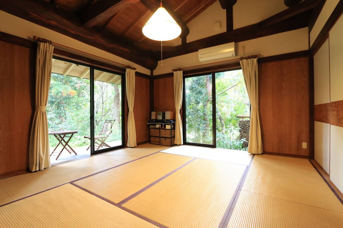 Une pièce de style japonais traditionnel, avec un sol recouvert de tatamis, des portes coulissantes et une vue sur la verdure environnante.