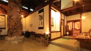 A traditional Japanese interior with tatami flooring, a large tree trunk, and wooden beams. - Sen-no-ie (Yakushima)