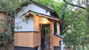 A wooden cabin with a stone fireplace, surrounded by trees. - Sen-no-ie (Yakushima)