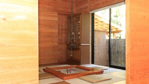 A wooden interior with a glass door leading outside, a wooden floor, and a small wooden table with a mat. - Sen-no-ie (Yakushima)