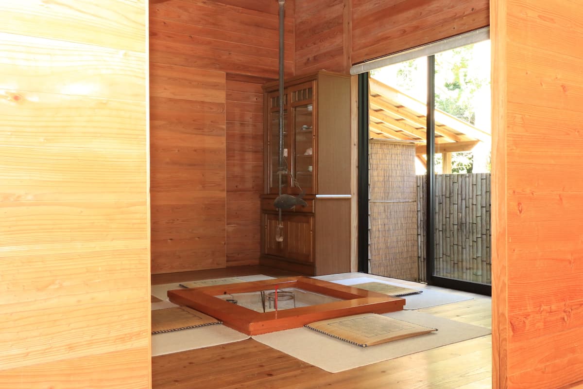 Un intérieur en bois avec une porte vitrée donnant sur l’extérieur, un plancher en bois et une petite table en bois surmontée d’un tapis.