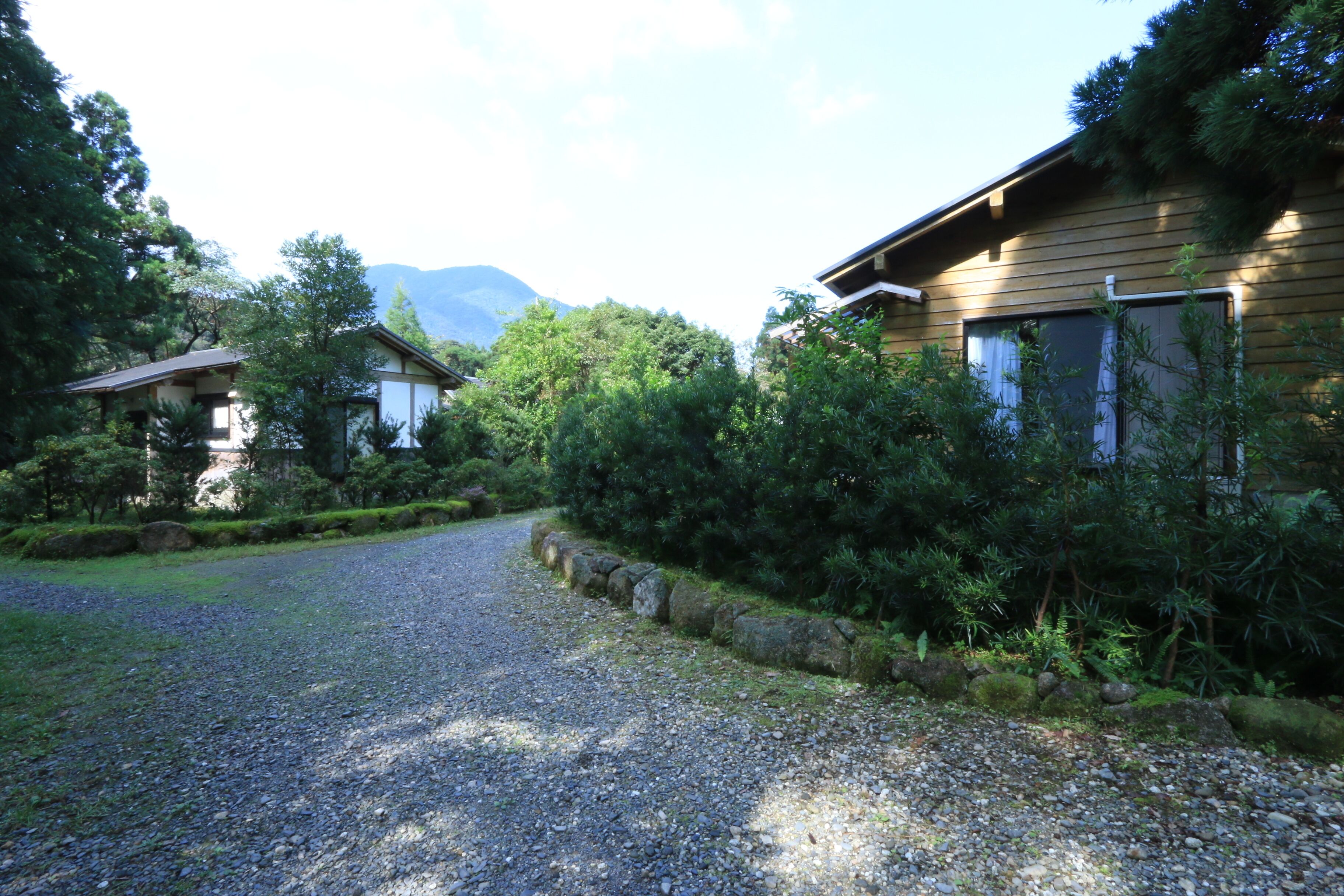 Ein Kiesweg führt zu einem Holzhaus mit einem Berg im Hintergrund.