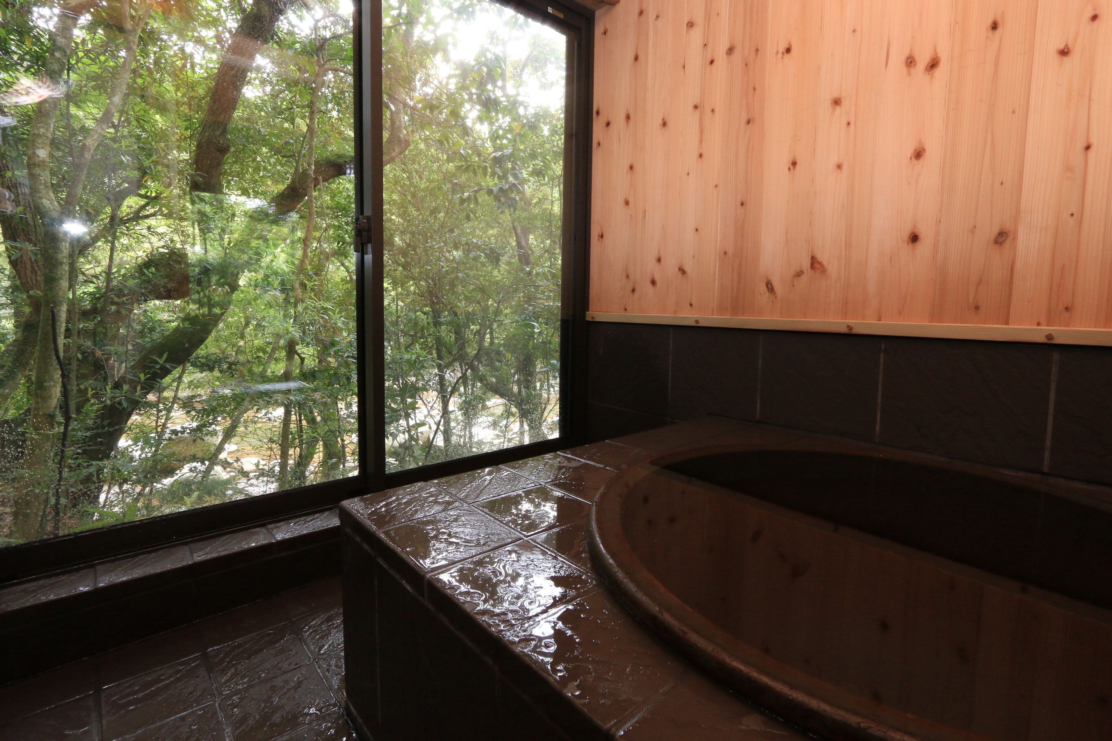 Un baño con un ventanal grande, pared de madera y bañera.
