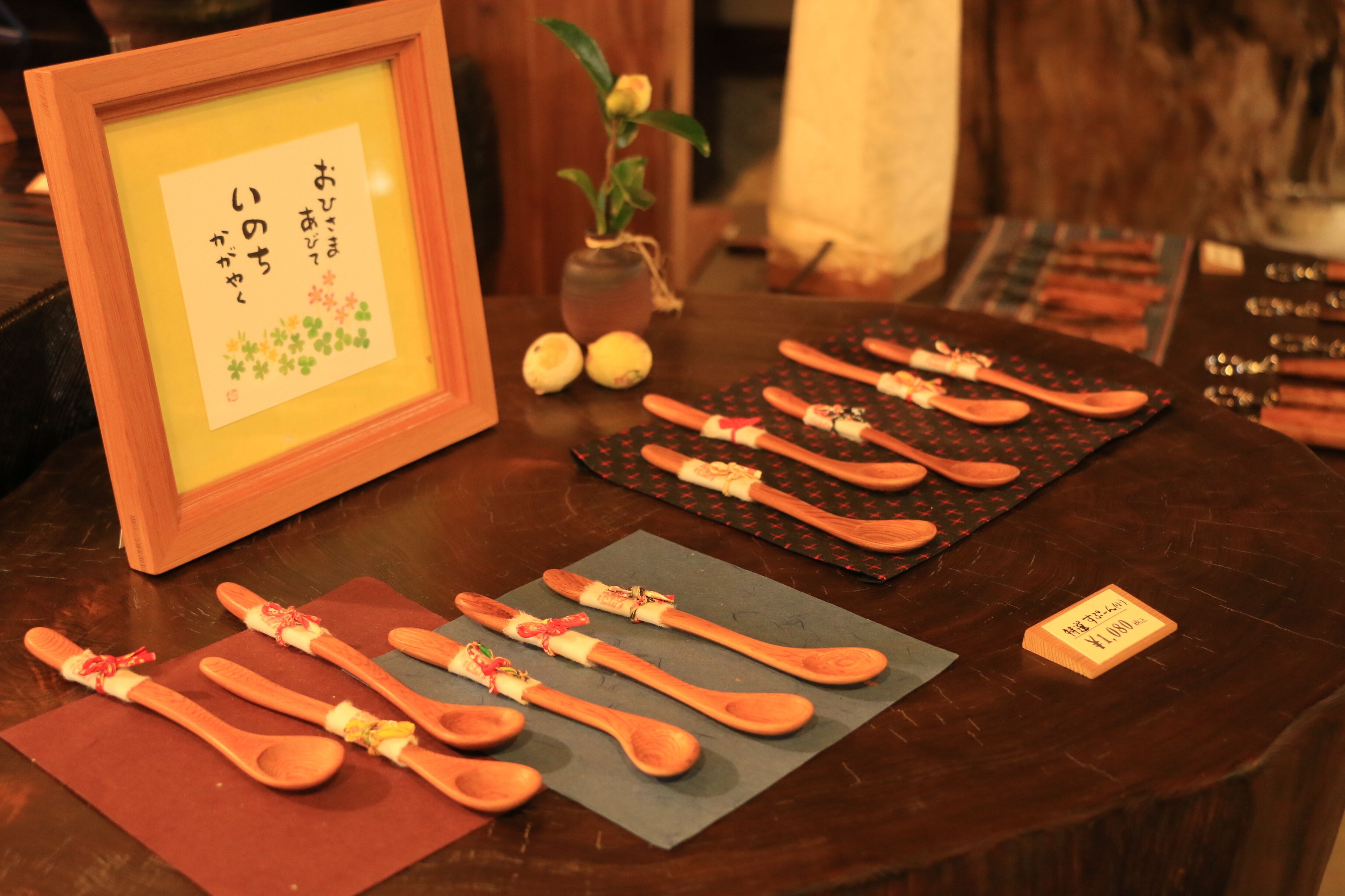 Una mesa de madera con varias cucharas de madera y un marco con texto japonés.