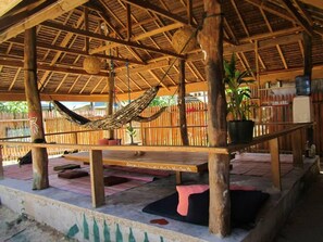 A covered outdoor seating area with a hammock, wooden tables, and a bench. - Paglaom Hostel - Adults Only (General Luna)