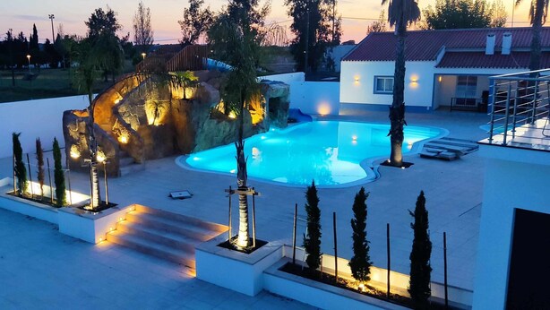 Ein Pool mit Felsen und Stufen, umgeben von einem weißen Gebäude und Bäumen.