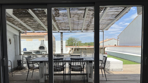 An outdoor patio with a wooden table and chairs, a grill, and a pergola.
