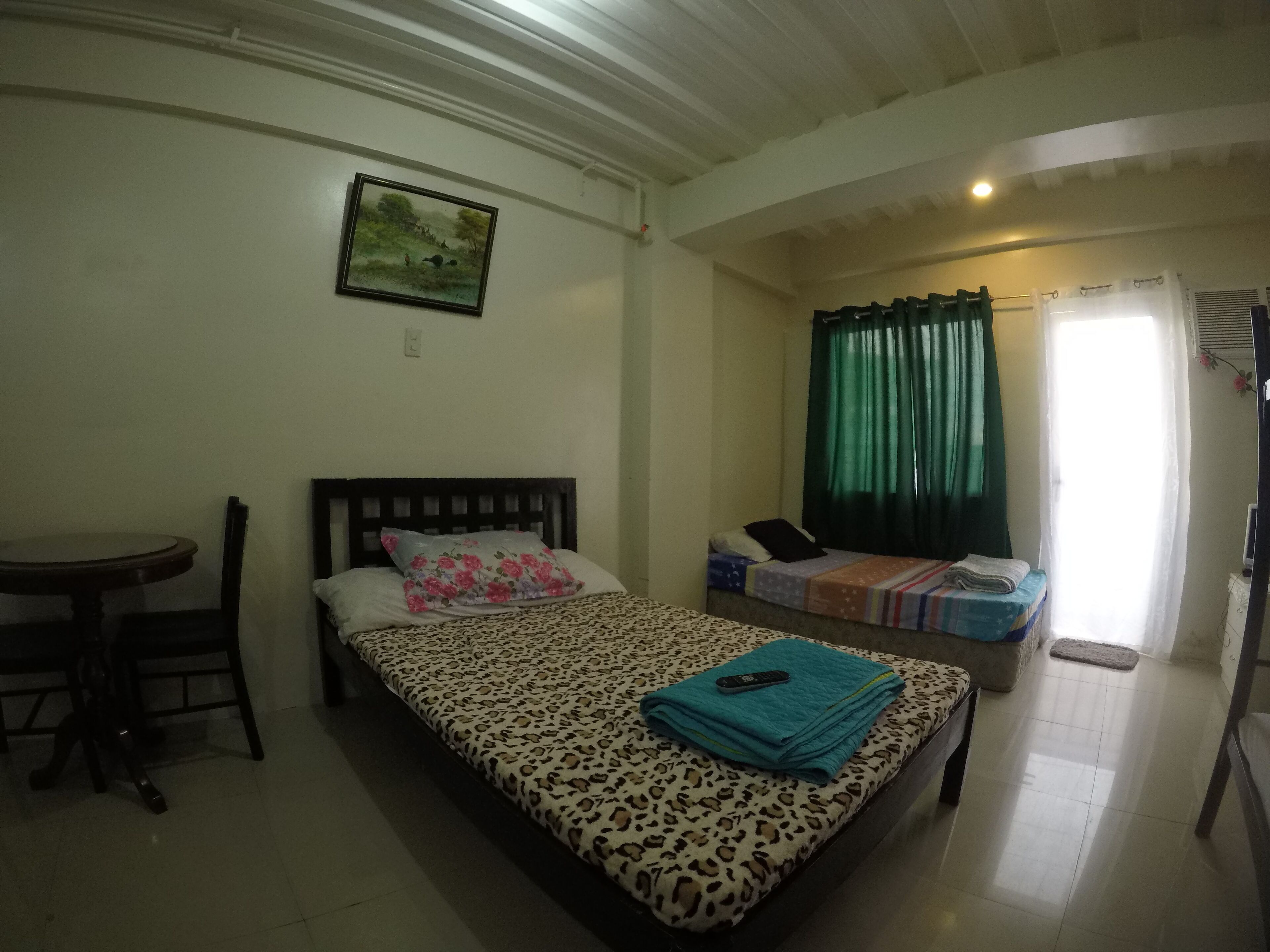 A bedroom with a bed, a chair, a small table, a window with curtains, and a picture on the wall.