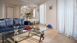 Una sala de estar moderna con una mesa de centro de vidrio, un sofá azul con cojines estampados y un comedor al fondo.