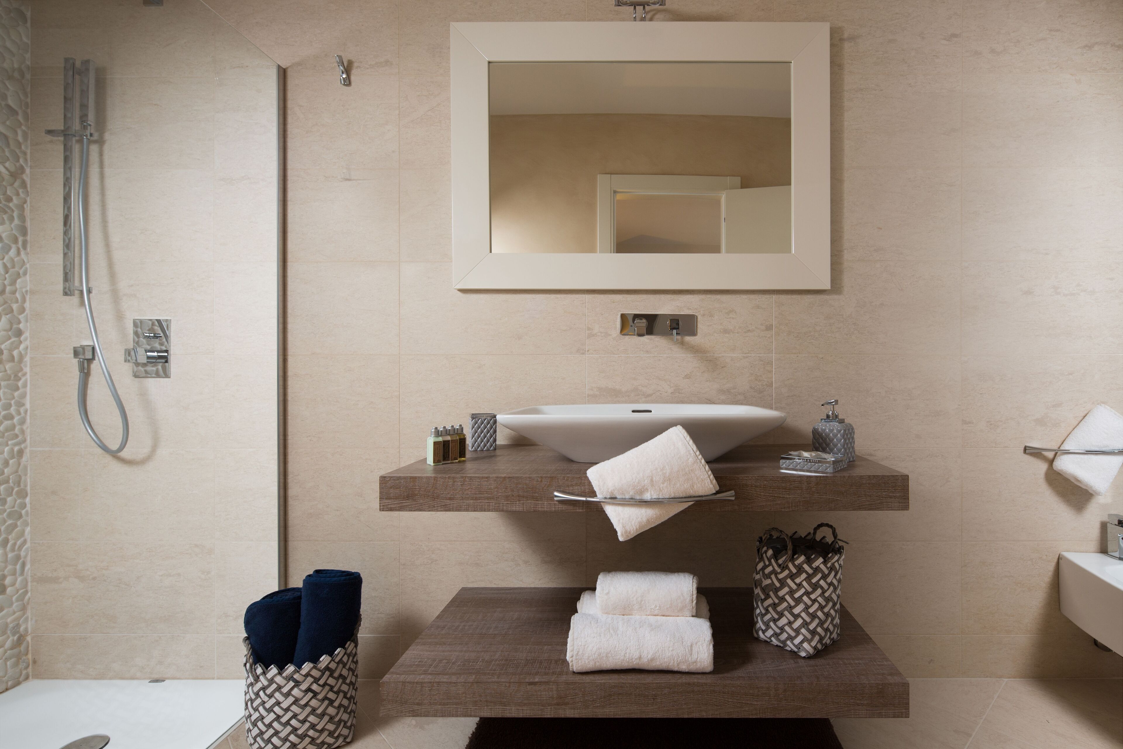A modern bathroom with a large mirror, a sink, and a shower. There are towels and toiletries on the counter.