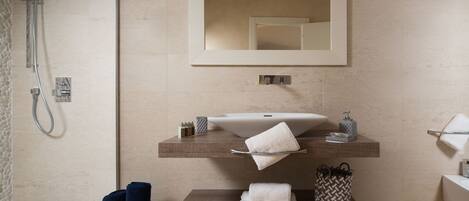 A modern bathroom with a large mirror, a sink, and a shower. There are towels and toiletries on the counter.
