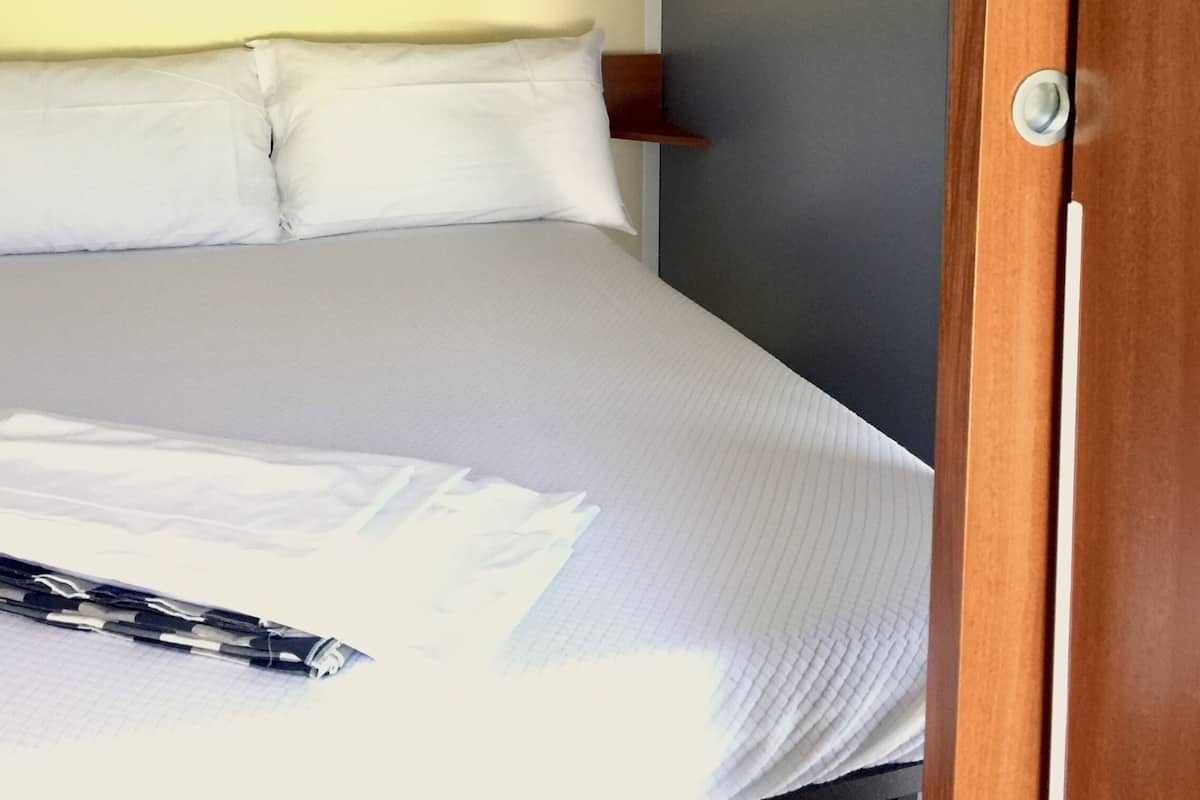Un lit bien fait, avec du linge de lit blanc et des oreillers, une tête de lit en bois et un mur gris.