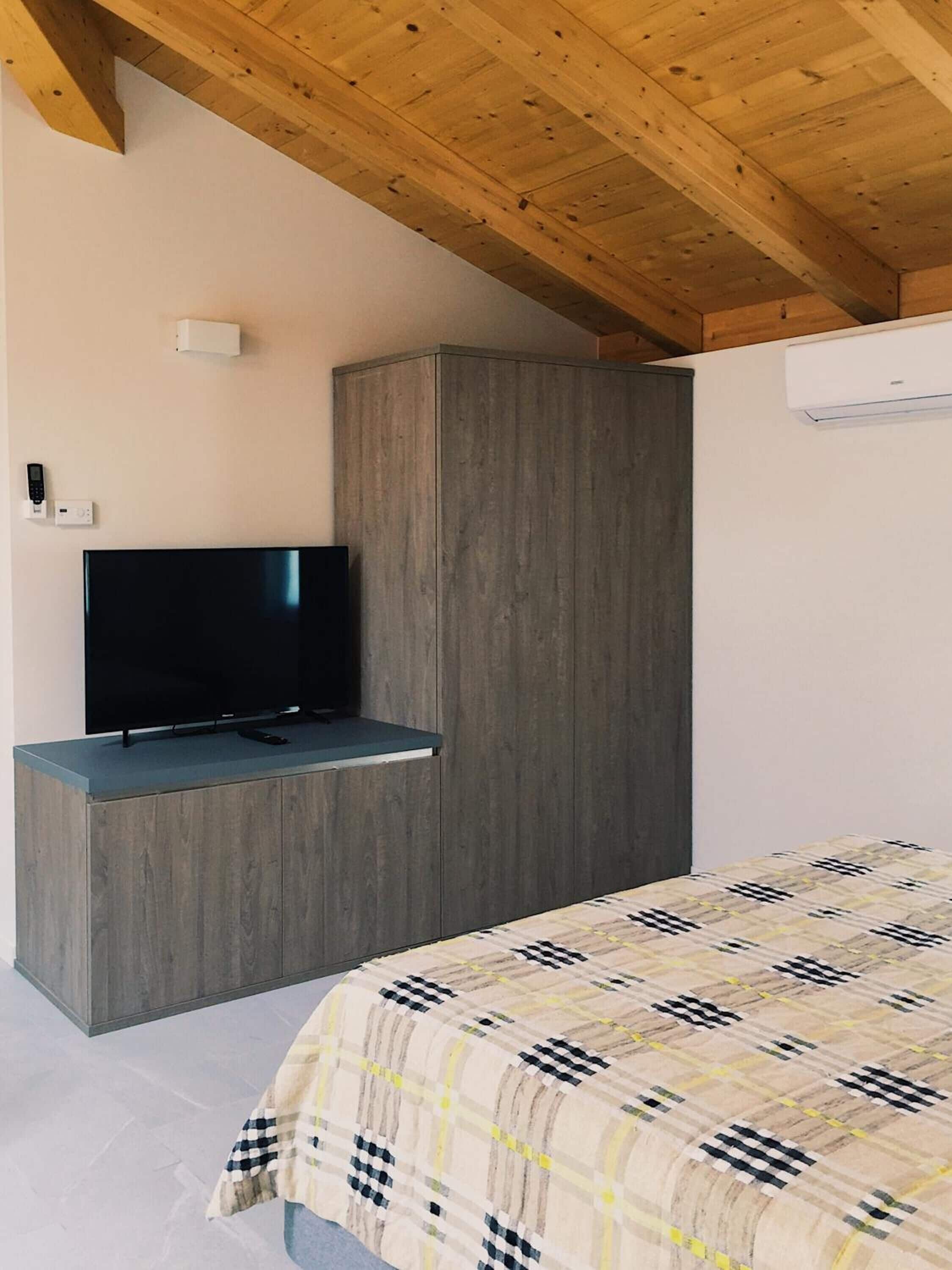 A bedroom with a bed, a TV on a wooden cabinet, and an air conditioner on the wall.