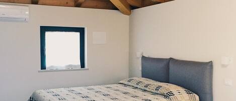 A bedroom with a bed, a window, and a wooden ceiling.