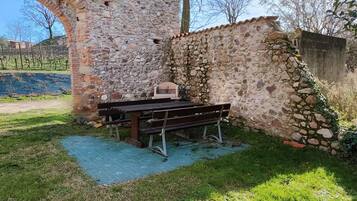 A stone wall with a wooden bench and a small table, surrounded by grass and a blue mat.