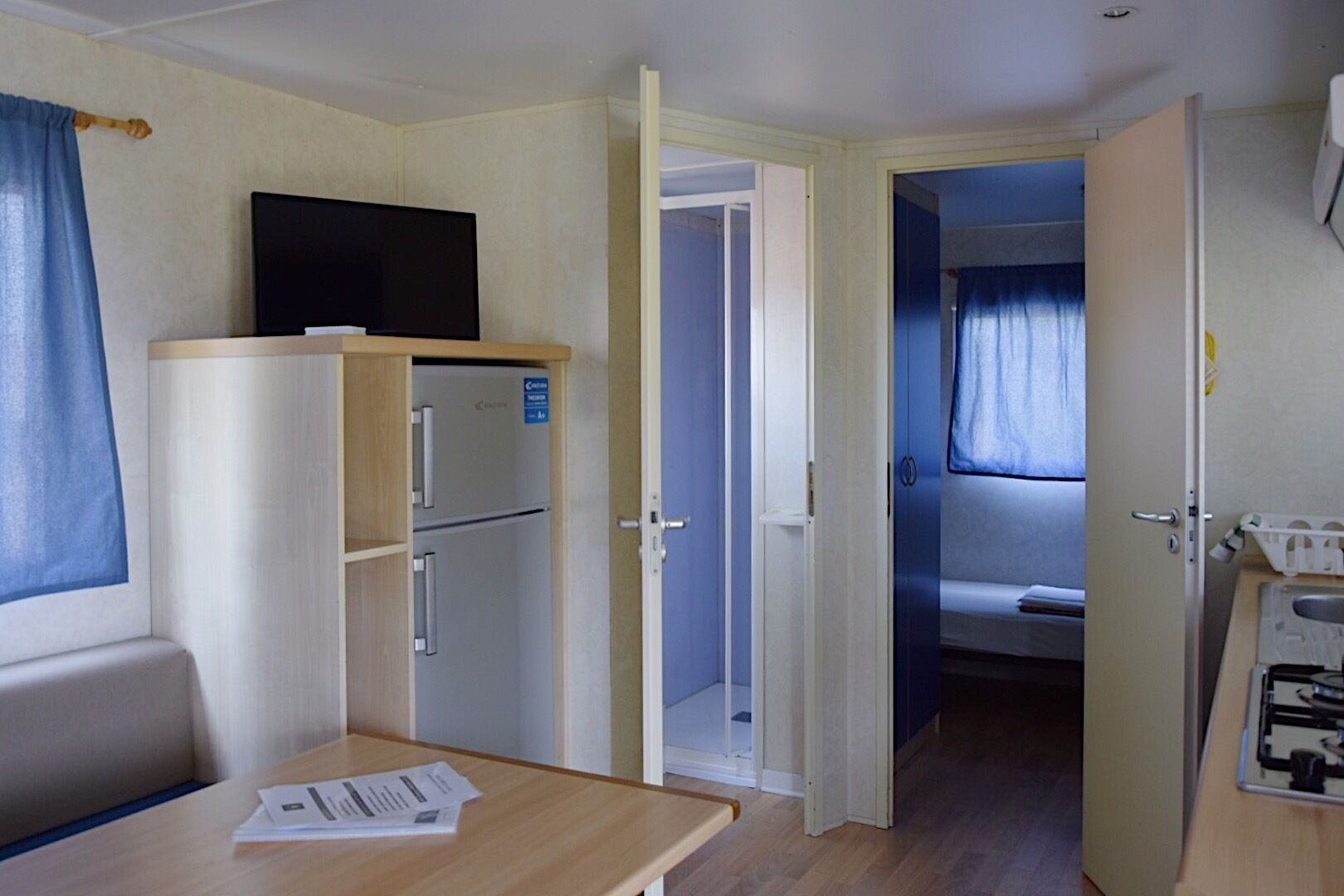 A compact room with a kitchenette, a bed, and a small table with papers.
