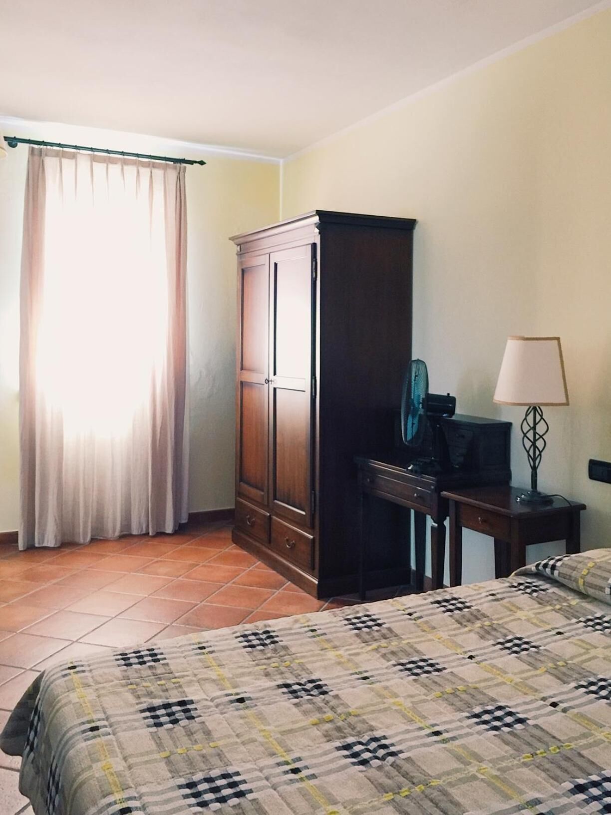 A bedroom with a bed, a desk with a chair, a wardrobe, and a lamp.