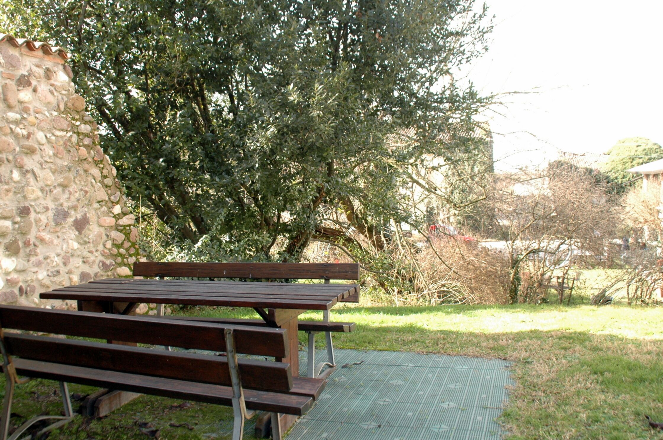 Un tavolo da picnic con panche, un muro in pietra e un grande albero sullo sfondo.