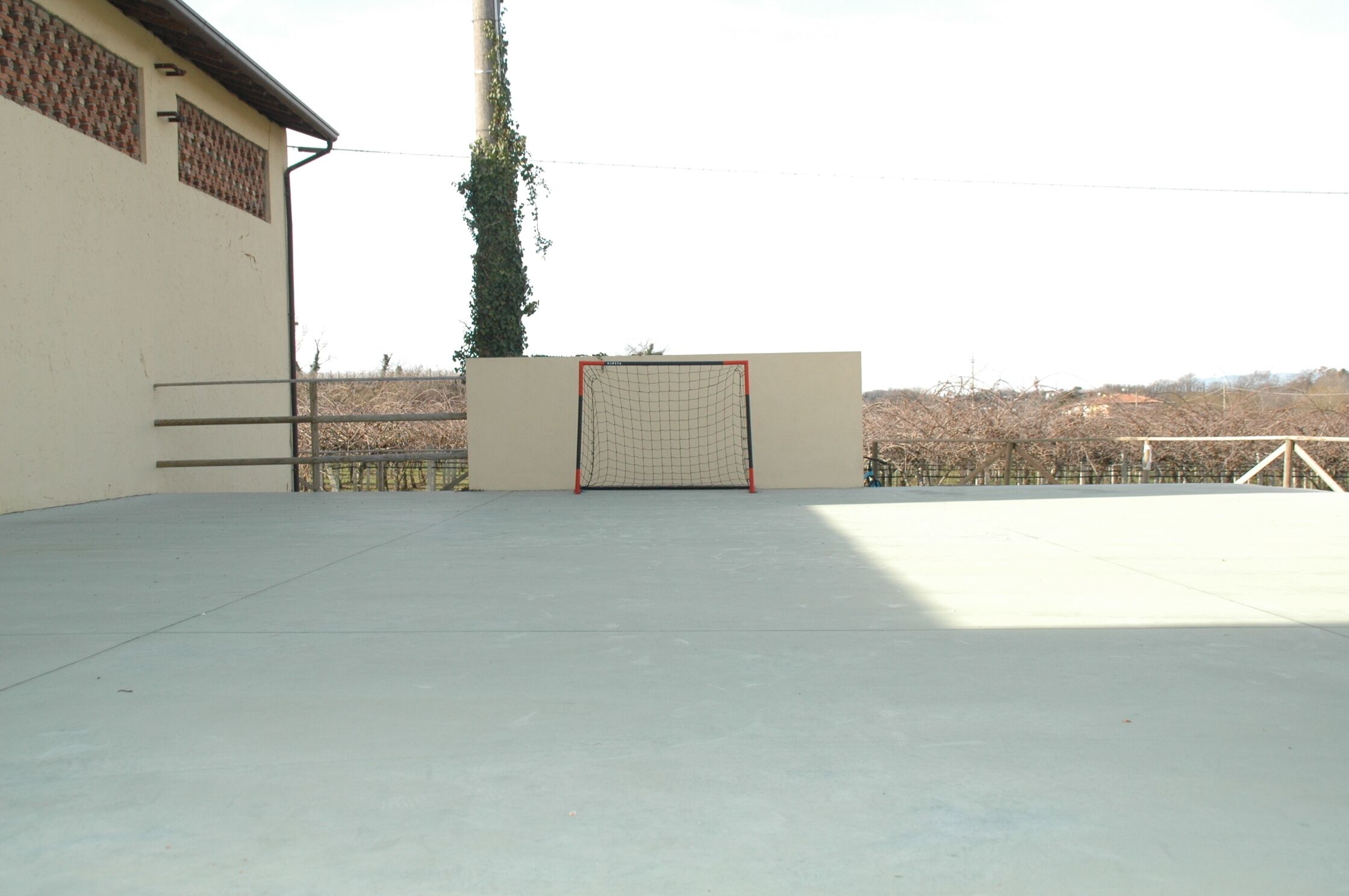An empty outdoor sports court with a goalpost, a building with a brick pattern, and a tree.